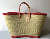 front view of straw tote showing weave pattern, red trim, leather handles, brand tag