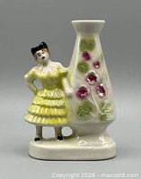 Front view of ceramic figural bud vase showing woman in yellow dress and floral vase section