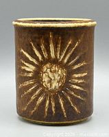 Front of brown glazed stoneware vase with cream sunburst design