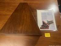 Closed triangular hardwood case beside provenance sheet