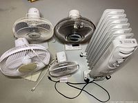 Four table fans and one oil-filled heater arranged on floor