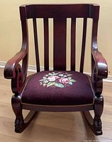 Front view of mahogany rocking chair showing slat back, carved arms, floral upholstered seat