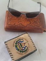 Storm sunglasses resting on brown tooled leather pouch, El Salvador wallet in foreground