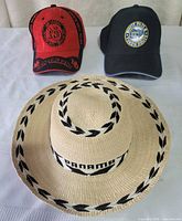 Front view of all three hats: straw Panama hat, red New Orleans cap, dark White Pass Yukon Route cap