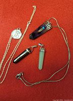 Necklaces and pendants laid out: amethyst pendant on chain, Sweetheart 16 charm on chain, two aventurine prism pendants