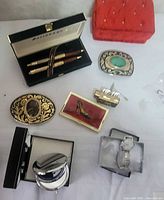 Group view showing all items: pen set, watch, cufflinks, belt buckles, lipstick holder, card case, compact mirror, red velvet case