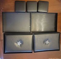 Five empty coin cases laid out closed: three small square, two larger rectangular with maple leaf lids