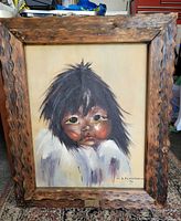 Front view of framed acrylic painting showing Inuit child portrait, artist signature R. Flaviani 76 and carved wood frame