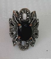 Front view of ornate silver-tone ring with black resin stone on white fabric