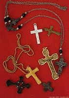 All seven cross pendants and necklaces laid out on red background
