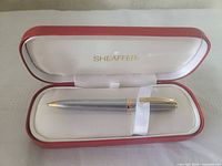 Pen resting in open Sheaffer case showing interior logo and gold-plated trim