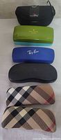 Front view of six stacked eyeglass cases showing brand logos and colors
