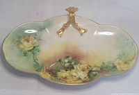 Top view of porcelain serving dish showing hand-painted yellow roses and gold handle