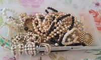 Tangled grouping of numerous faux pearl and bead necklaces in a plastic bin