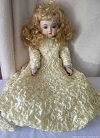 Full view of doll seated showing entire rosette gown and blond curls