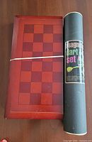 closed wooden folding chessboard beside storage tube for magnetic dart set