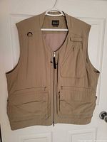 Front view of khaki utility vest showing zipper closure, multiple front pockets, D-ring and chest pocket detail