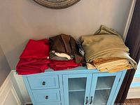 Stacks of folded red, brown, and green table linens on blue cabinet