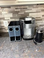 Coffee maker, two pod holders, milk frother on countertop
