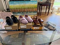 All three pairs—black slipper, pink slipper, brown sandals—on table