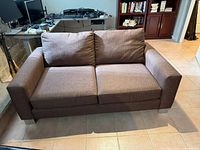 Front view of brown upholstered loveseat showing cushions, arms, and legs