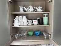 Cabinet view showing floral tea set, multiple mugs, Bodum cups, travel tumbler, and stemless wine glasses