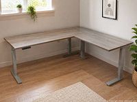 Full view of assembled L-shaped desk in room, showing grey laminate top, metal legs, keypad