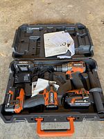 Open hard case showing both tools, two batteries, charger and manuals