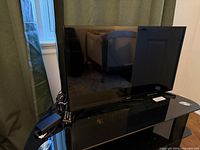 Front view of Samsung 32-inch TV on stand with remote and power cable visible
