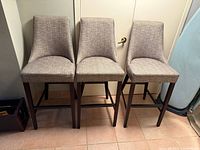 Front view of three matching grey upholstered bar stools