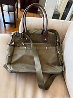 Front view of olive green nylon shoulder bag with brown leather handles and green webbing strap