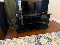 Front view of black glass TV stand with three shelves