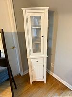 Full view of white tall cabinet front with glass door and lower storage