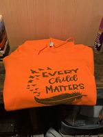Folded orange hoodie with Every Child Matters graphic visible