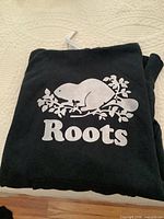 Front view showing Roots beaver logo on folded black hoodie