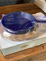 Shrink-wrapped blue cast iron skillet resting on hardwood base