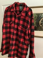 Full view of red/black plaid Woolrich shirt on hanger