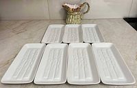Six white asparagus motif plates and one asparagus pitcher grouped on counter