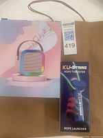 Karaoke speaker retail box beside KU-STRING rope launcher box