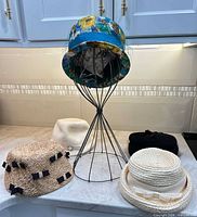 Group shot of all five hats around metal stand