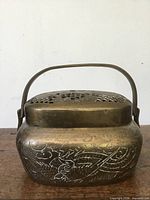 Front view of brass potpourri container showing embossed bird/floral design and swing handle