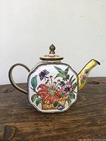 Front view of enamel teapot showing main floral and insect design