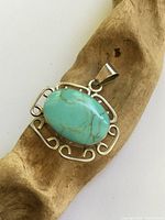 Front view of pendant on driftwood, shows turquoise stone and silver scroll frame