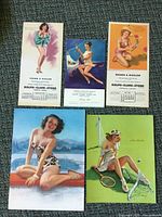 Five pin-up prints laid out on carpet