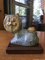 Side view of drip-glaze ceramic lion on wooden base