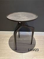 Front view of dark grey cast metal accent table showing round top and three-leg base