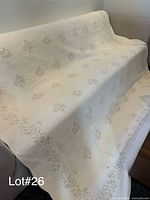 Full view of quilt draped over sofa showing size, scalloped edge, embroidery