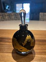 Perfume bottle with stopper inserted, showing gold leaf design