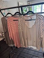 Three Cabi tops on hangers: gray tunic, peach-pink striped dolman, cream-black striped V-neck