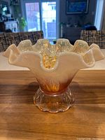 Front view of opalescent marigold carnival glass footed bowl showing color gradient and ruffled rim